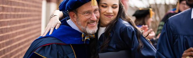 A man and a women embracing each other smiling in their graduation regalia 